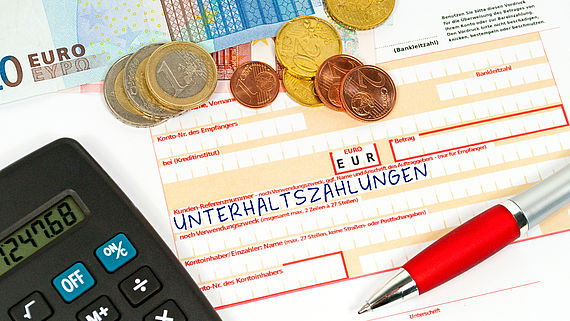 Taschenrechner und Muenzen liegen auf einem Ueberweisungsbeleg