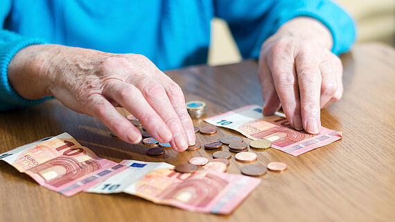 Alte Frau zaehlt Geld, das auf dem Tisch liegt