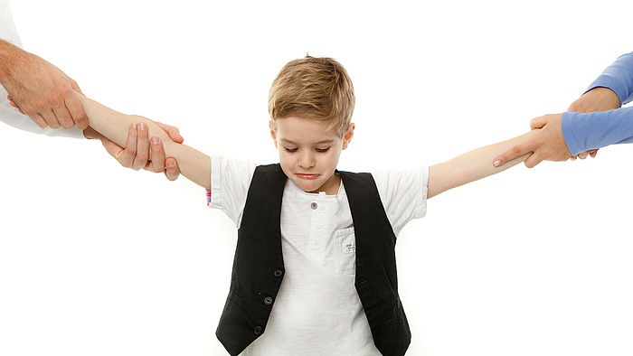 Kleiner Junge wird an jeweils einem Arm von einem Elternteil gezogen