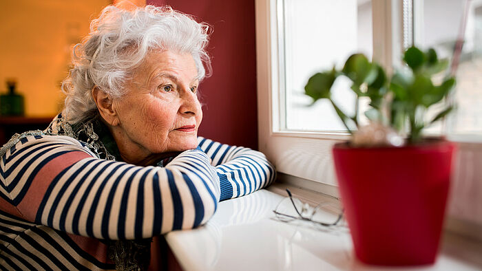 Eine alte Frau sitzt traurig vor dem Fenster