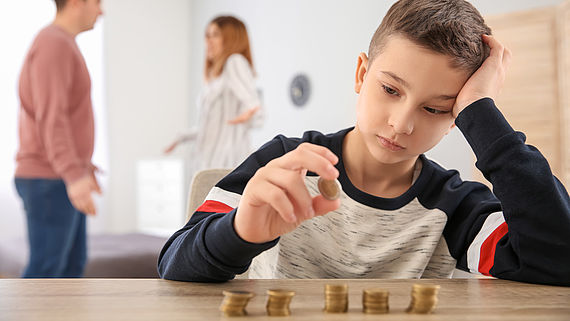 Trauriger Junge zaehlt Geld waehrend sich die Eltern streiten