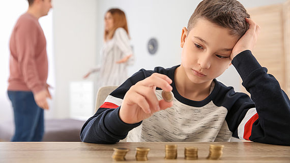 Trauriger Junge zaehlt Geld waehrend sich die Eltern streiten