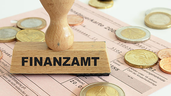 Muenzen und ein Stempel vom Finazamt liegen auf einer Lohnsteuerkarte und