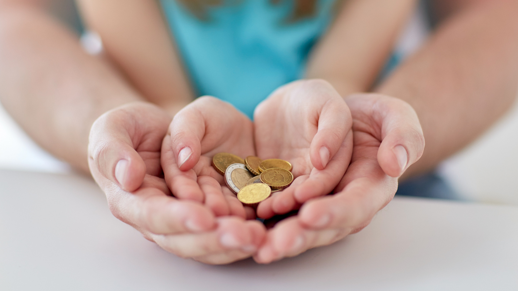 Nahaufnahme von Familienhaenden, die Euro-Geldmuenzen halten