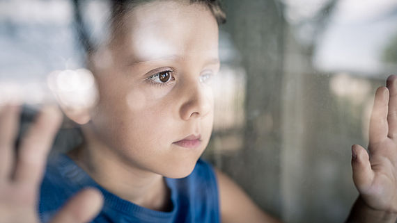 Junge schaut traurig aus dem Fenster