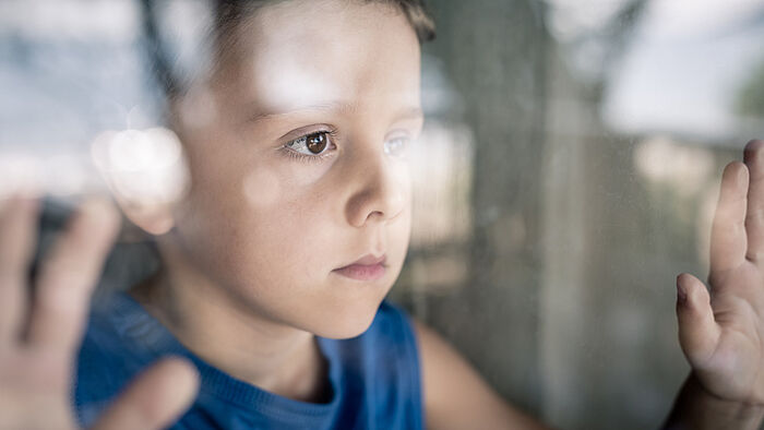Junge schaut traurig aus dem Fenster
