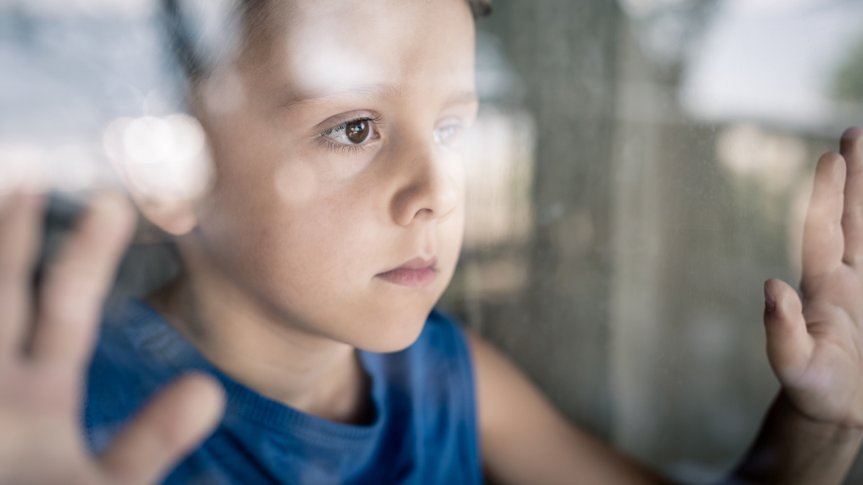 Junge schaut traurig aus dem Fenster
