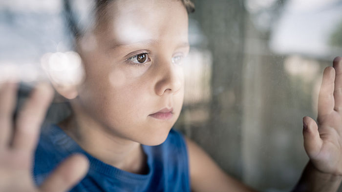 Junge schaut traurig aus dem Fenster