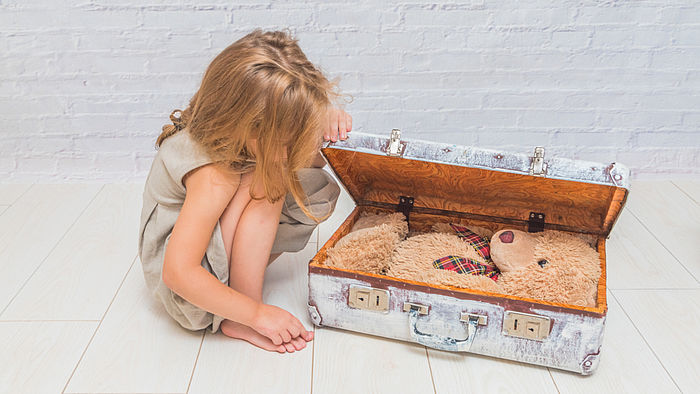 Maedchen vor einem Koffer mit einem Teddybaeren