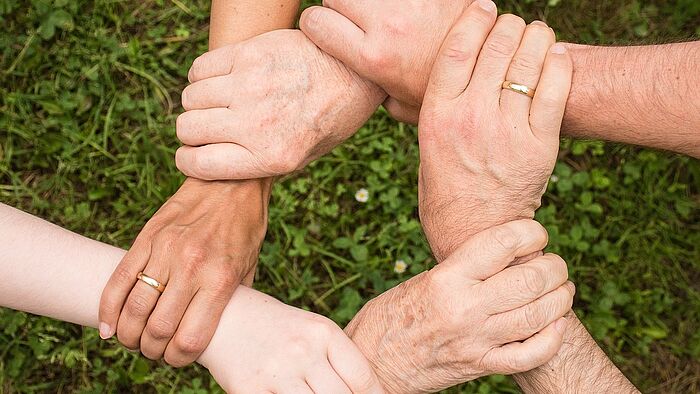 Aufnahme von Händen einer Familie die sich an den Handgelenken in Kreisform anfässt