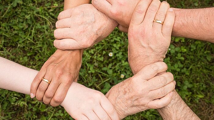 Aufnahme von Händen einer Familie die sich an den Handgelenken in Kreisform anfässt