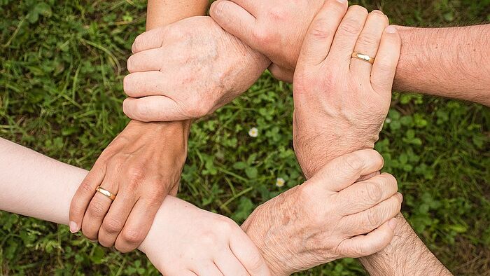 Aufnahme von Händen einer Familie die sich an den Handgelenken in Kreisform anfässt