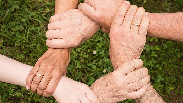 Aufnahme von Händen einer Familie die sich an den Handgelenken in Kreisform anfässt