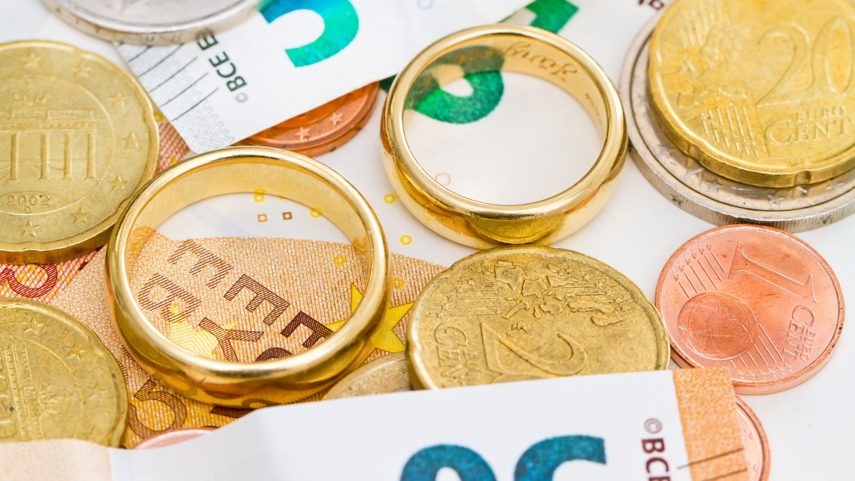 Eheringe liegen zwischen Euro-Banknoten und Muenzen