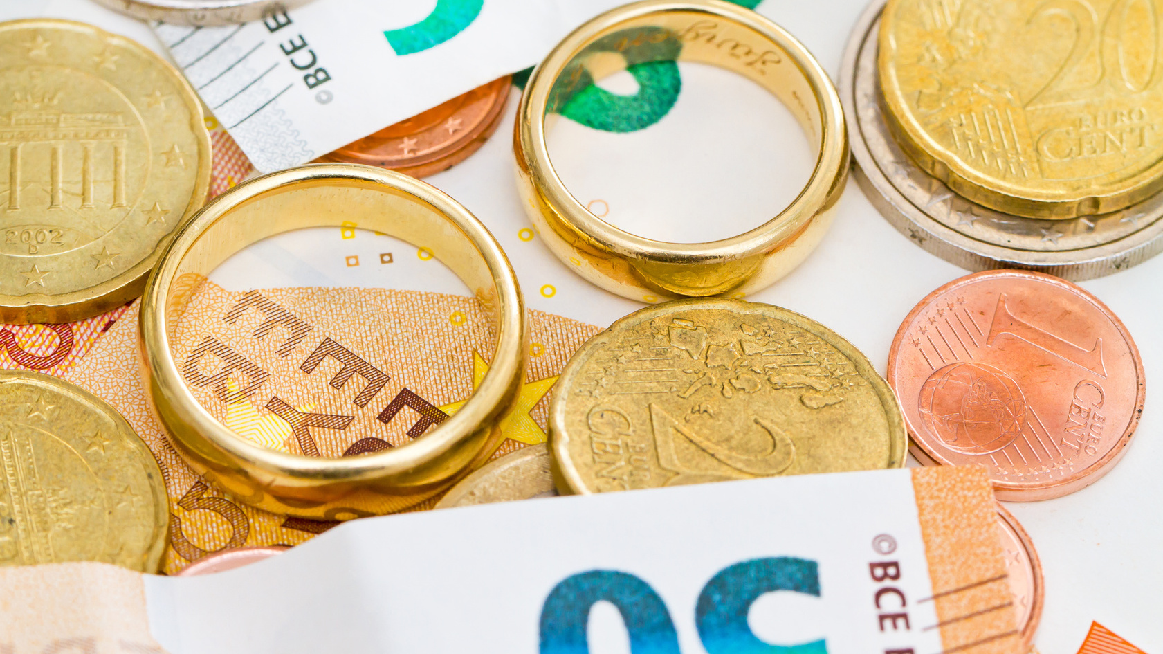 Eheringe liegen zwischen Euro-Banknoten und Muenzen