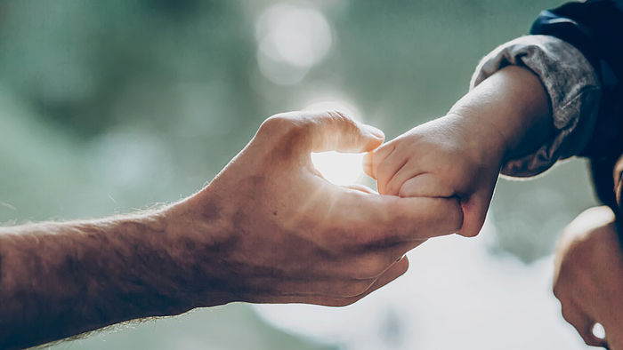 Vater und kleiner Sohn halten Hände im Sonnenlicht