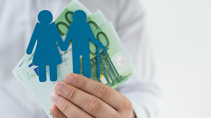 Eine Person hält einen Scherenschnitt von einem älteren Paar zusammen mit Geldscheinen